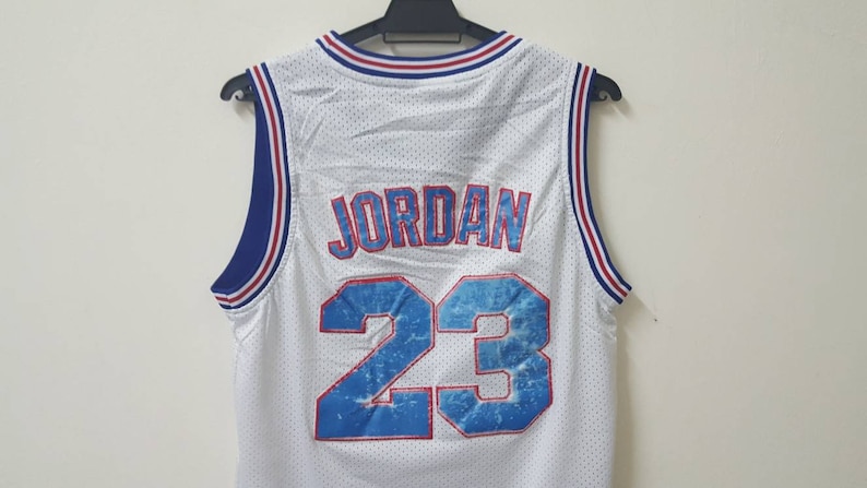 May include: White basketball jersey with blue and red trim. The back of the jersey has the name "JORDAN" and the number "23" in a blue and white design.