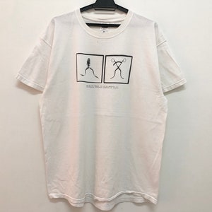 Peut inclure: T-shirt blanc avec un imprimé graphique noir et blanc de deux figures. Le texte "We do not brand our products, we brand our people." est imprimé sous le graphique.