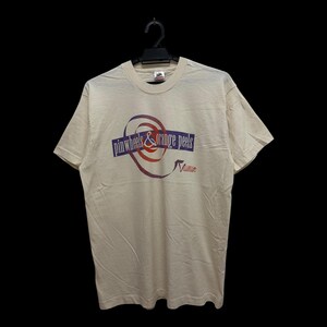 Puede incluir: Una camiseta de manga corta color crema con un diseño gráfico en el pecho. El gráfico incluye un elemento en espiral rojo y morado con el texto "pinwheels & orange peels" en una banda morada y la palabra "Volume" en rojo debajo.