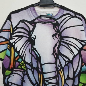 Puede incluir: Camiseta blanca con un gr&aacute;fico de elefante de estilo vitral colorido.