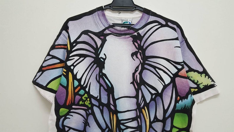 Puede incluir: Camiseta blanca con un gr&aacute;fico de elefante de estilo vitral colorido.