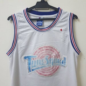 May include: White basketball jersey with red and blue trim. The jersey has a large graphic of the "Tune Squad" logo with a basketball and the words "Tune Squad" in a blue and white font.