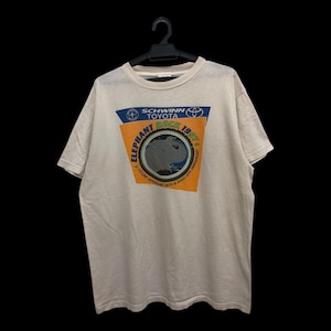 May include: A beige t-shirt featuring a graphic with the text "Schwinn Toyota Elephant Rock 1997". The graphic includes an elephant silhouette and a bicycle wheel design. The shirt is hanging on a black hanger.
