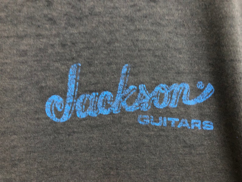 May include: A blue and white logo on a dark gray background that reads "Jackson Guitars".