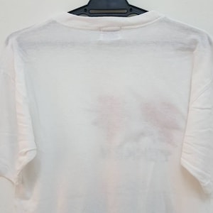 May include: White short-sleeved t-shirt with a faded graphic print on the back.
