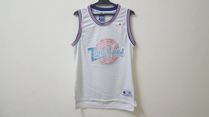May include: White basketball jersey with blue and red trim. The jersey has a large graphic of the Tune Squad logo with the text "Tune Squad" in blue and white.