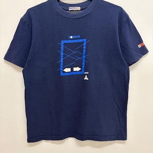 Puede incluir: Camiseta azul marino con un diseño gráfico. El diseño incluye la palabra "BRAWLS" encima de un rectángulo azul con flechas y líneas blancas. El año "2000" está impreso debajo. La camiseta tiene mangas cortas y cuello redondo.