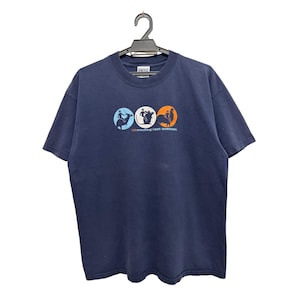 May include: Navy blue t-shirt with a graphic of three colored circles. Each circle contains a silhouette of a person in action. The text "...STATE UNIVERSITY" is below the circles. The shirt is hanging on a black hanger.