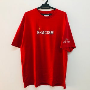 Puede incluir: Camiseta roja con el texto "ERACISM" impreso en la parte delantera y "STOP THE HATE" en la manga.
