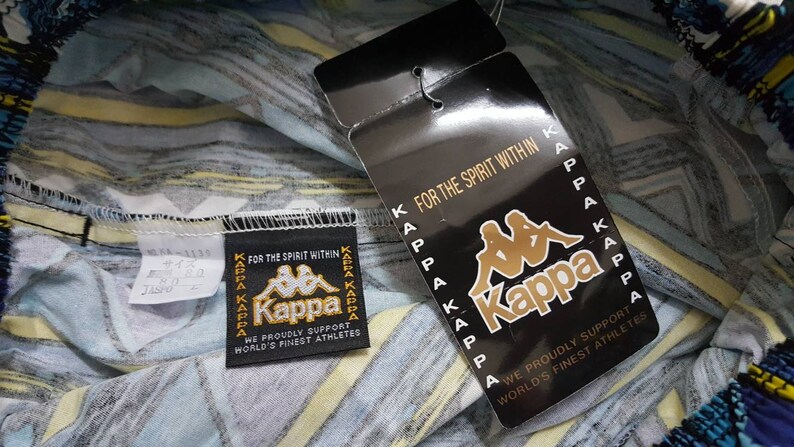 May include: A white, blue, and yellow patterned fabric with a black and white Kappa logo tag. The tag reads "For the spirit within" and "We proudly support world's finest athletes".