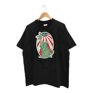 May include: Black t-shirt with a green and red graphic of the Statue of Liberty holding a torch and a book. The graphic is surrounded by a red, white, and blue circle with a Masonic symbol in the center.
