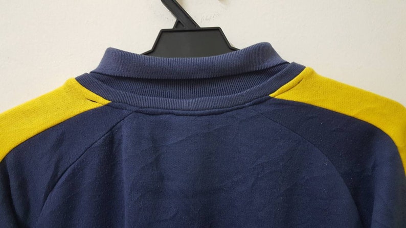 May include: A navy blue sweatshirt with yellow accents on the shoulders. The sweatshirt has a mock neck collar.