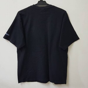 K&ouml;nnte beinhalten: Ein schwarzes T-Shirt mit kurzen &Auml;rmeln, das an einem schwarzen Kleiderb&uuml;gel h&auml;ngt. Die R&uuml;ckseite des T-Shirts ist sichtbar, mit einem kleinen Textdetail am linken &Auml;rmel. Das T-Shirt ist aus einem weichen Material.