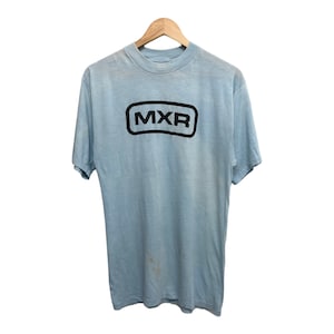 Puede incluir: Una camiseta azul claro con un logotipo "MXR" negro en un rectángulo.
