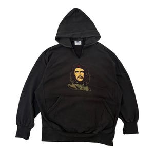 May include: Black hooded sweatshirt with a portrait of Che Guevara on the front. The sweatshirt has a kangaroo pocket and a drawstring hood. The graphic is in shades of brown, green, and red.