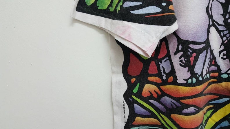 Puede incluir: Camiseta blanca con un estampado gr&aacute;fico abstracto de colores. El dise&ntilde;o presenta una variedad de formas y colores, incluyendo rojo, naranja, amarillo, verde, azul y morado. El gr&aacute;fico parece ser una representaci&oacute;n estilizada de una persona o un grupo de personas.