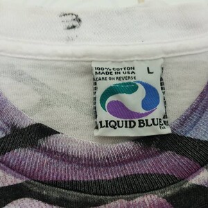 Puede incluir: Camiseta blanca con estampado abstracto morado, negro y blanco. La camiseta tiene una etiqueta de Liquid Blue con el texto "100% algod&oacute;n hecho en EE. UU. cuidado en el reverso" y una talla L.