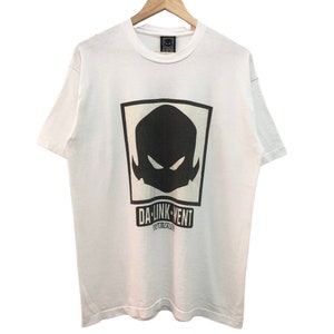May include: White t-shirt featuring a black and white graphic of a stylised face with the text "DA-UNK-VENT" underneath.