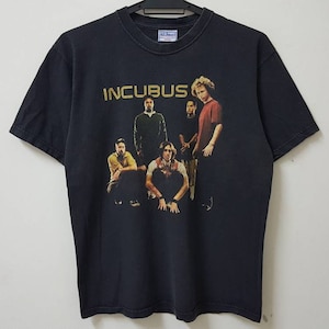 May include: Black t-shirt with a band graphic featuring the band Incubus. The band members are pictured in a group photo with the band name in gold lettering.