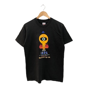 May include: Black t-shirt featuring a graphic of a yellow face with a blue hat and one eye. The text "SMUG" is printed below the graphic. The text "A UNEXPECTED TURN OF EVENTS" is printed below the word "SMUG".