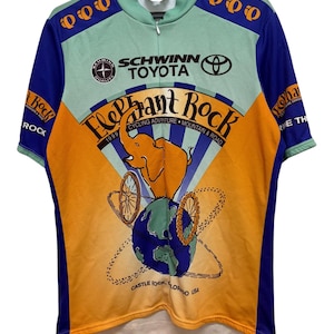 May include: A short-sleeve cycling jersey in light green, orange, and blue. The front features the text "Elephant Rock 1999 Cycling Adventure Mountain & Road," a graphic of an elephant on a globe, and logos for Schwinn and Toyota.
