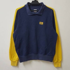 May include: A navy blue sweatshirt with yellow sleeves and a small yellow patch on the chest that says "NIKE".
