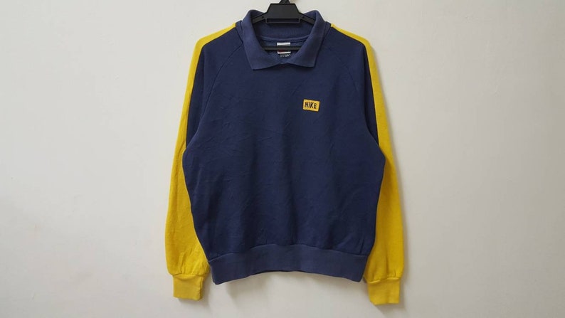 May include: A navy blue sweatshirt with yellow sleeves and a small yellow patch on the chest that says "NIKE".
