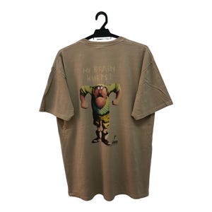 May include: A tan t-shirt with a cartoon character graphic on the back. The character is a man with a large head and a surprised expression. The text "My Brain Hurts!" is printed above the character.