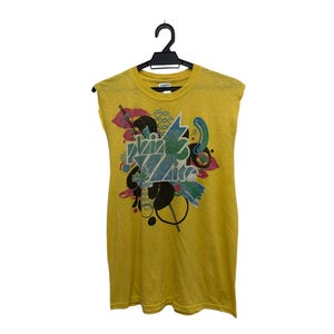 Puede incluir: Camiseta sin mangas amarilla mostaza con un diseño gráfico colorido. El diseño incluye el texto "ZZZ Lite" en una fuente estilizada, junto con formas y patrones abstractos en varios colores. La camiseta está colgada de una percha negra.