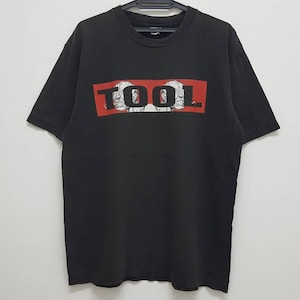 May include: Black t-shirt with a red rectangle and the word "TOOL" in white letters. The rectangle has a graphic of two faces inside.