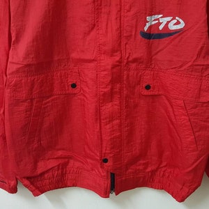 May include: Red windbreaker jacket with a white and blue logo that says "FTO". The jacket has two pockets with black buttons and a zipper closure.