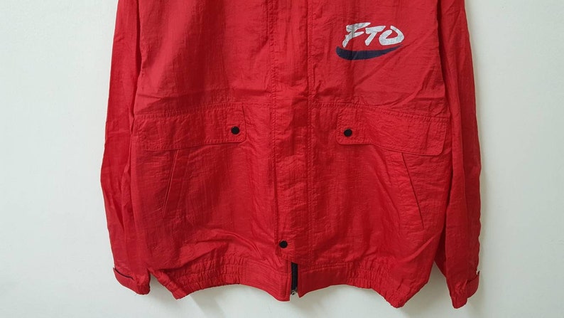 May include: Red windbreaker jacket with a white and blue logo that says "FTO". The jacket has two pockets with black buttons and a zipper closure.
