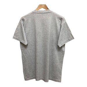 Op de afbeelding: Een grijs t-shirt met korte mouwen. Het t-shirt hangt aan een houten hanger.