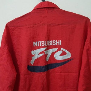 May include: Red long-sleeve jacket with a white "MITSUBISHI FTO" logo on the back. The logo is in a stylized font with a blue swoosh underneath.