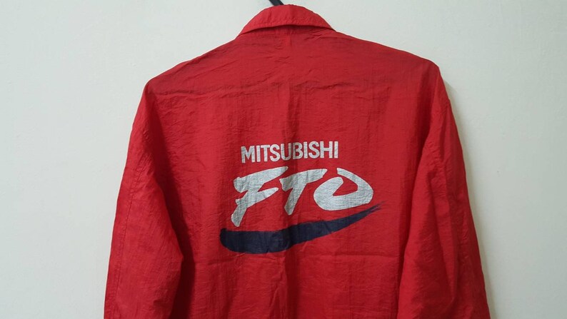 May include: Red long-sleeve jacket with a white "MITSUBISHI FTO" logo on the back. The logo is in a stylized font with a blue swoosh underneath.