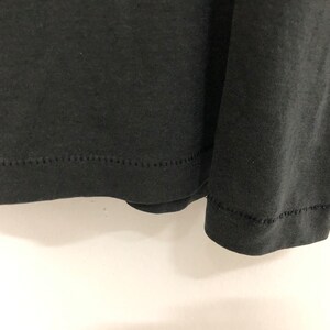 May include: Close-up of the bottom hem of a black long-sleeved shirt. The hem is stitched with a zig-zag stitch.