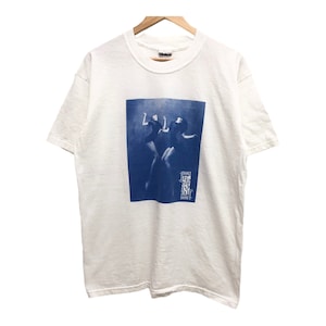 May include: White t-shirt with a blue graphic of silhouetted figures and the text "Strange Fruit Dance". The shirt is hanging on a wooden hanger against a white background. The t-shirt has short sleeves and a crew neck.