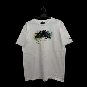 May include: White t-shirt with a colorful graphic design featuring the text "MTV Video Music Awards 05". The design includes black, blue, yellow, and green elements. The shirt is hanging on a black hanger.