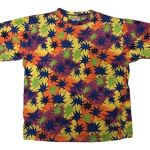 May include: A short-sleeved t-shirt with a vibrant, all-over pattern. The design features a repeating motif of starburst shapes in a mix of colors, including yellow, orange, blue, green, and purple. The shirt is made of a soft material.