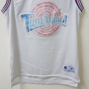 May include: White basketball jersey with a blue, red, and white "Tune Squad" logo on the front. The jersey is made of mesh fabric and has a Champion logo on the bottom right.