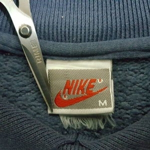 May include: A close-up of a blue Nike sweatshirt with a white tag that says "NIKE" in red lettering and "M" for size.