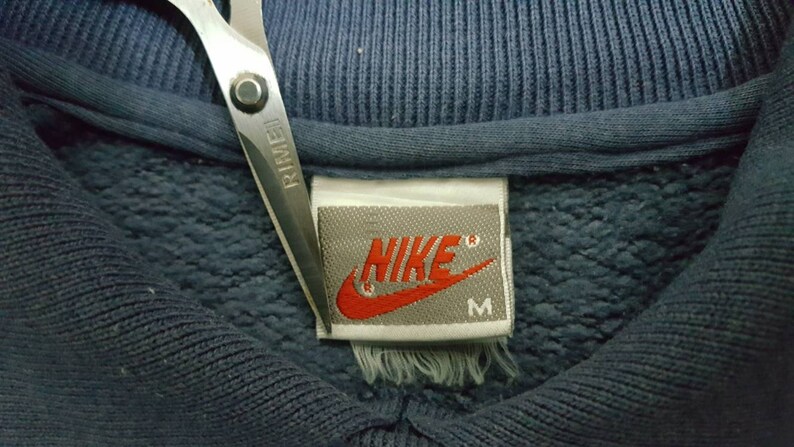 May include: A close-up of a blue Nike sweatshirt with a white tag that says "NIKE" in red lettering and "M" for size.
