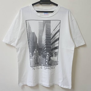 May include: White t-shirt with a black and white photo print of a person walking down a city street. The text "NICE SHOES" is printed below the photo.