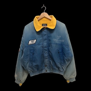 May include: A blue and yellow jacket with a Gauloises logo and a Honda Racing patch. The jacket has a zipper closure and a yellow fleece lining.