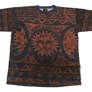 May include: A brown and blue short-sleeved t-shirt with a tribal pattern and a sun face design.