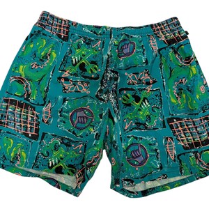 May include: Teal-colored shorts with an elastic waistband and a vibrant, patterned design. The pattern includes green, black, and pink shapes, along with a hand gesture symbol. These shorts are a fun and colorful addition to any wardrobe.