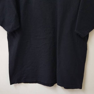 K&ouml;nnte beinhalten: Ein schwarzes T-Shirt mit kurzen &Auml;rmeln. Der &Auml;rmel tr&auml;gt das Wort "PRAGUE" in blauen und roten Buchstaben. Das T-Shirt ist aus einem weichen, dunklen Stoff gefertigt und wird vor einem schlichten wei&szlig;en Hintergrund pr&auml;sentiert.