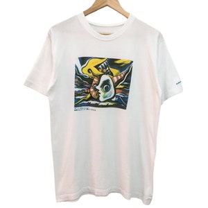 May include: White t-shirt with a colorful abstract painting of a face on the front. The painting is in shades of blue, yellow, red, and green. The text "The Chromatic Moment of Blue Green" is printed below the painting.