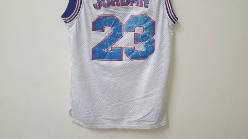 May include: White basketball jersey with blue and red trim. The back of the jersey has the number 23 in blue with a water-like design.