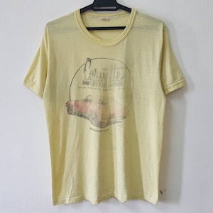 May include: Yellow short-sleeved t-shirt with a vintage graphic of a red Corvette convertible car. The graphic includes the text "Corvette" and "Road America".